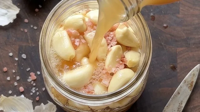 Garlic cloves and pink salt in a jar being covered with liquid